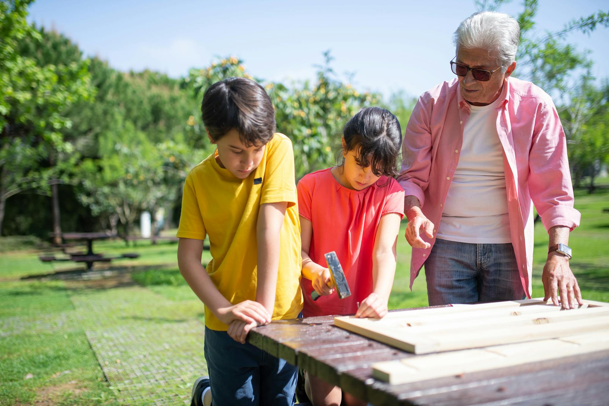 2 children work on a woodworking project as an adult looks on.